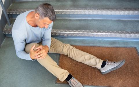 Mann hält sich nach Sturz von einer Treppe das schmerzende Knie